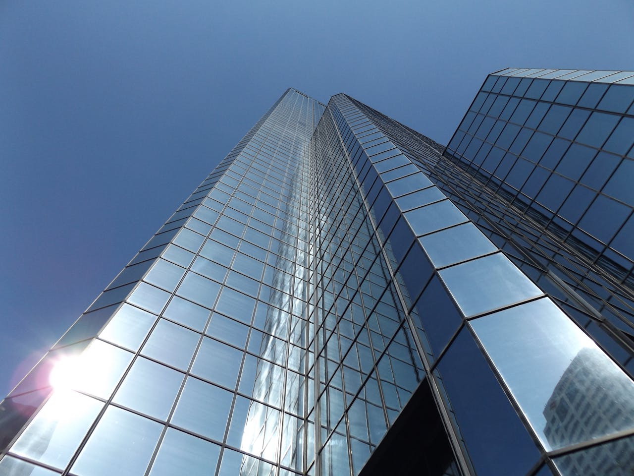 Upward view of a glass skyscraper reflecting the blue sky and sunlight, epitomizing modern urban architecture.